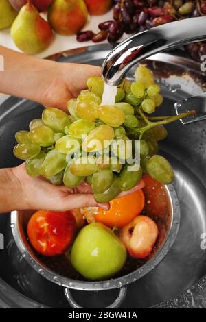 Mani donna lavando uva e altri frutti in colino nel lavandino Foto Stock