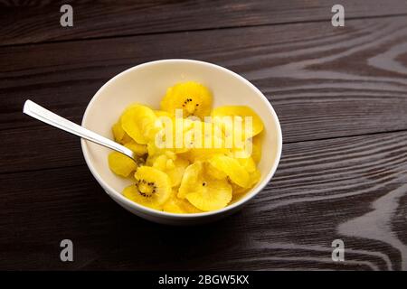 Fette di frutta Kiwi Gold in ciotola bianca con cucchiaio. Kiwi a fette con carne gialla in piatto di insalata su sfondo di legno. Frutta sana succosa matura Foto Stock