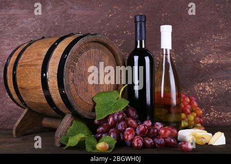 Vino in bottiglia, formaggio Camembert e brie, uva e botte di legno su tavola di legno su sfondo legno Foto Stock