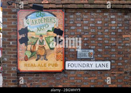 Segno che fa pubblicità al pub delle armi del giardiniere sul muro di mattoni vicino al segno di Foundry Lane a Lewes, East Sussex Foto Stock