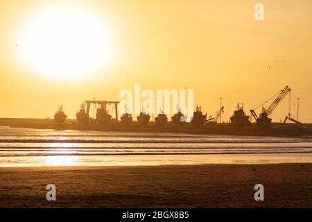 Tramonto sulla spiaggia di Essaouira Marocco con barche ormeggiate in un cantiere navale Foto Stock