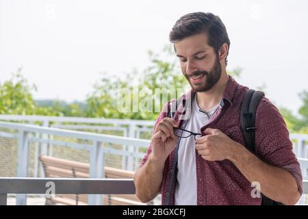 Un hipster bearded che indossa un bottone rosso giù camicia che togli leggermente gli occhiali per vedere più chiaramente che cosa è nella distanza con una stella diritta Foto Stock