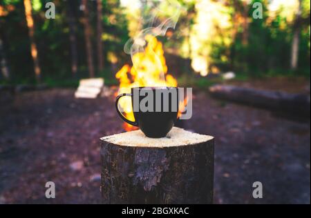 Caffè arrosto fumante in Mug nero vicino a fiamme in campeggio Foto Stock