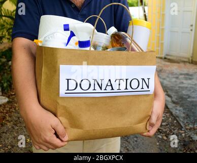 Un volontario consegna una borsa di donazione riempito con cibo e di pulizia durante il Covid-19 / Coronavirus Pandemic Foto Stock