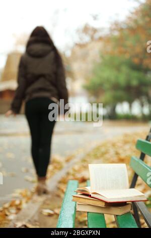 Libro a sinistra sulla panchina con silhouette di ragazza a piedi nel parco autunnale Foto Stock