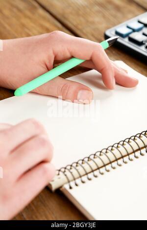 Mano femminile con penna, notebook e calcolatrice su sfondo di tavolo in legno Foto Stock