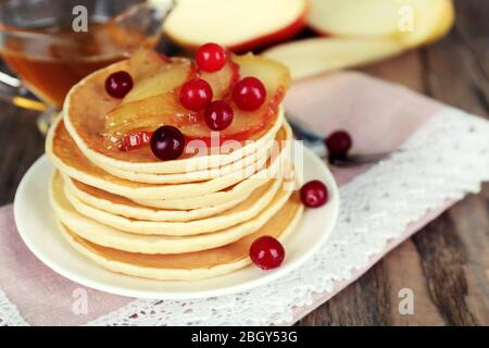 Pila di deliziosi pancake con fette di mela e bacche sul piatto e tovagliolo su sfondo di legno Foto Stock