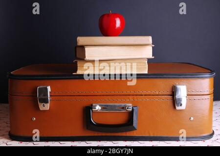 Valigia vintage con pile su libri su superfici a motivi geometrici e sfondo scuro Foto Stock