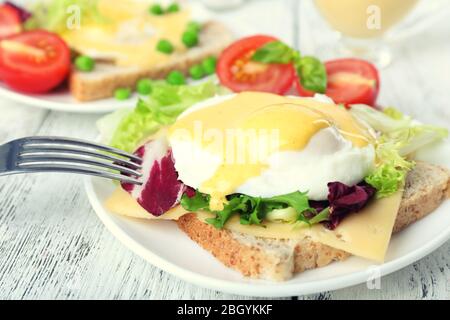 Toast con uovo Benedetto e pomodoro su piatto su tavola di legno Foto Stock