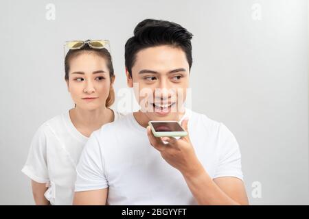 Ritratto di una giovane coppia utilizzando i telefoni cellulari, mentre in piedi insieme su sfondo grigio, curiosa donna che guarda mans telefono Foto Stock