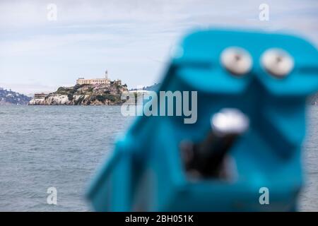 Primo piano dell'isola di Alcatraz nella baia di San Francisco, con un binocolo a moneta blu in primo piano Foto Stock