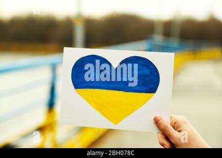 Mano che tiene carta cuore con dipinto bandiera Ucraina Foto Stock