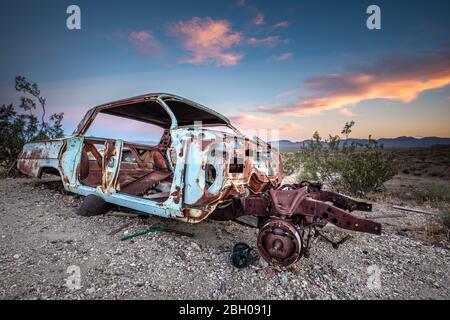 Un'auto di berlina rovinata e arrugginita nella città fantasma di Rhyolite, Valle della morte, al tramonto Foto Stock