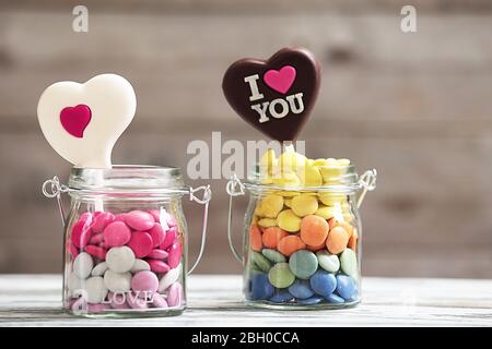 Caramelle dolci in vaso di vetro con cuori su sfondo di legno Foto Stock