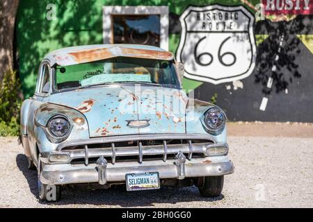 Primo piano di una vettura d'epoca arrugginita di colore azzurro parcheggiata, di fronte a un graffito della Route 66 Foto Stock