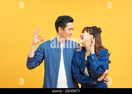 Giovane bella coppia in piedi su sfondo giallo isolato facendo gesto ok con mano sorridente, con faccia felice. Foto Stock