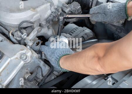 Il meccanico dell'auto sta esercitando una chiave dinamometrica a manico lungo con una mano che indossa un guanto per riparare e mantenere il motore dell'automobile. Foto Stock