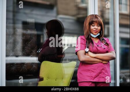 Medico femminile afro-americano presso l'uniforme da laboratorio rosso in maschera facciale protettiva. Medicina, professione e concetto di salute. Foto Stock