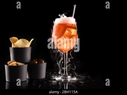 Bellissimo cocktail isolato su sfondo nero con ghiaccio secco fumo. Vapore bianco in fresco vetro freddo, con antipasti e spazio per testi. Ideale per Foto Stock