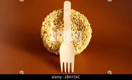 Tagliatelle istantanee crude a forma di cerchio con forchetta a perdere in legno. Pasta, per la preparazione della quale è sufficiente versare acqua bollente e. Foto Stock