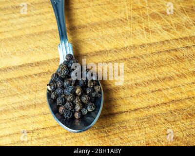 Un cucchiaino di pepe nero su un tagliere di legno Foto Stock