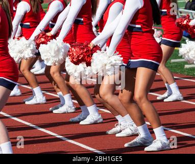 Cheerleaders della scuola superiore che si levano in piedi su una pista rossa che effettua una procedura con i poms rossi e bianchi del POM. Foto Stock