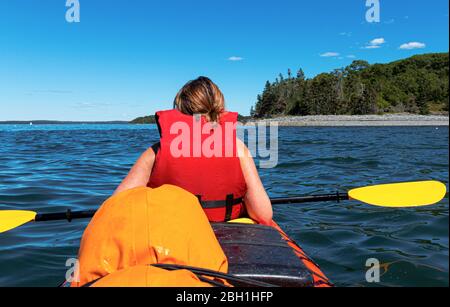 Primo piano di kayak femminile a frenchmans Bay Bar Harbor Maine da passanger dietro di lei con una delle isole porcupine in background. Foto Stock