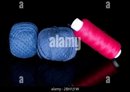 Gruppo di due rocchetti di filo blu intero con uno rosa isolato su vetro nero Foto Stock