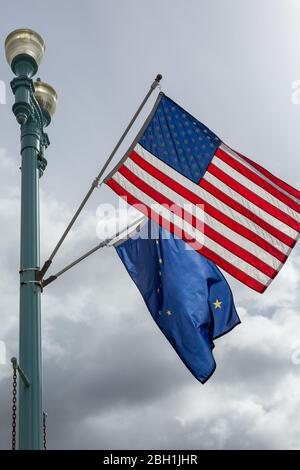 Stelle e strisce americane e la bandiera dell'Alaska soffiano nel vento contro un cielo drammatico Foto Stock