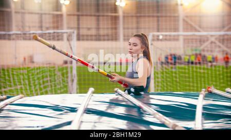 Pole vault training - una giovane bella donna che tiene un palo sopra i tappetini. Scatto intermedio Foto Stock