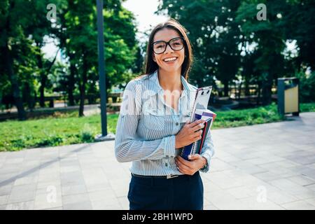 Studentessa sorridente con libri in un parco Foto Stock