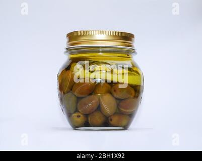 Un vaso di vetro riempito con olive biologiche fatte in casa in olio con limone, pepe nero e foglie di alloro Foto Stock