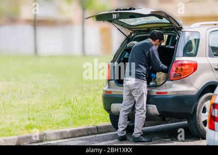 Persona che ritorna dallo shopping con l'auto che indossa guanti blu in lattice come misura di protezione dal coronavirus. Uomo con borse da shopping in arrivo h Foto Stock