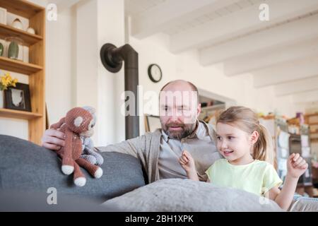 Padre e piccola figlia seduti insieme sul divano a casa giocando con i giocattoli Foto Stock
