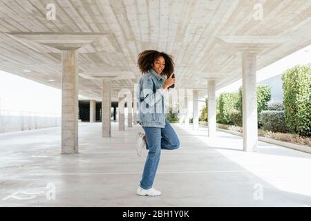 Giovane donna che balla mentre ascolta musica con auricolari e smartphone Foto Stock