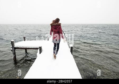 Vista posteriore di una giovane donna che corre sul molo innevato sul lago Starnberg, Germania Foto Stock