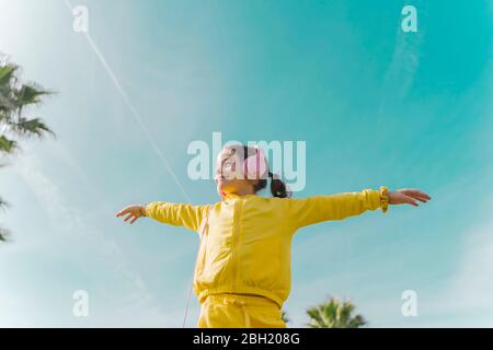 Ragazza piccola felice che indossa le braccia aperte ascoltando musica con le cuffie all'aperto Foto Stock