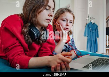 Ritratto di due sorelle con cuffie e computer portatile a letto Foto Stock