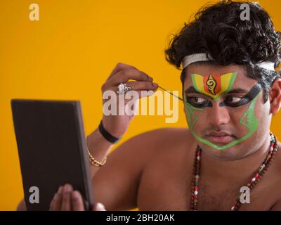 Ballerino di Kathakali che guarda nello specchio e applica il colore verde sul suo viso. Foto Stock