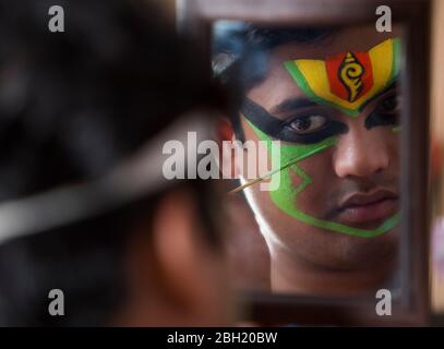 Ballerino di Kathakali che guarda nello specchio e applica il colore verde sul suo viso. Foto Stock