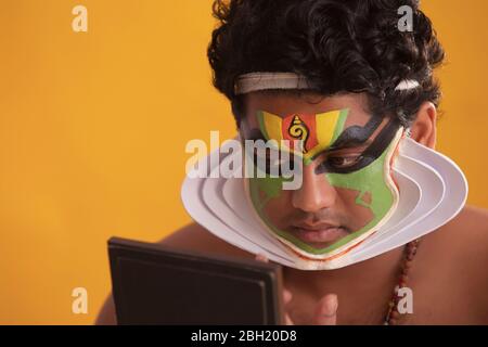 Ballerino di Kathakali che guarda nello specchio e controlla la forma di chutty sul suo viso. Foto Stock