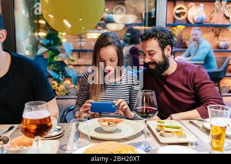 Donna che scatta foto del cibo con gli smartphone a cena con gli amici in un ristorante Foto Stock