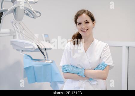 Dentista femminile in piedi in clinica con le braccia incrociate Foto Stock