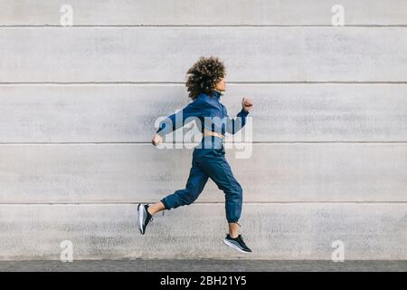 Giovane donna di stile che corre lungo parete di cemento Foto Stock