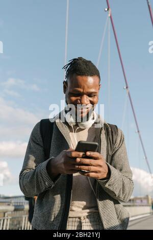 Ritratto di un uomo sorridente su un ponte con le cuffie utilizzando lo smartphone Foto Stock