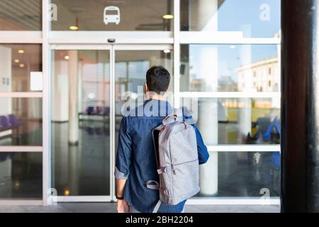 Vista posteriore dell'uomo con zaino davanti all'ingresso della stazione degli autobus Foto Stock