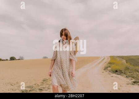 Donna seria in abito vintage che cammina su una strada remota campo in campagna Foto Stock