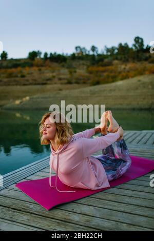 Giovane donna che fa yoga su un molo, posa arco Foto Stock