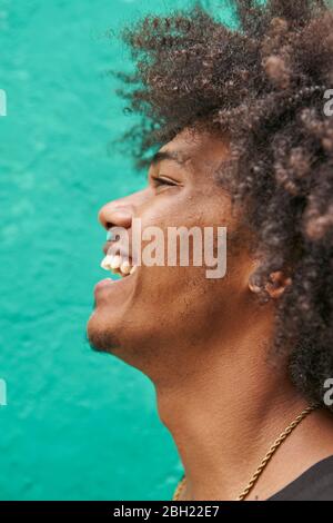 Profilo di ridere giovane con afro contro parete verde Foto Stock