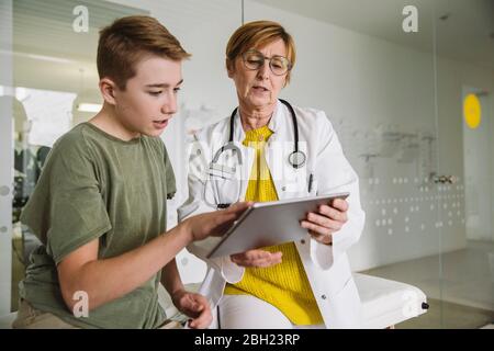 Medico che mostra la compressa al ragazzo adolescente in pratica medica Foto Stock